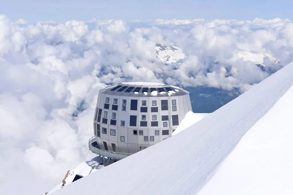 Futuristic circular building on snowy mountain peak above clouds, Gouter Hut.