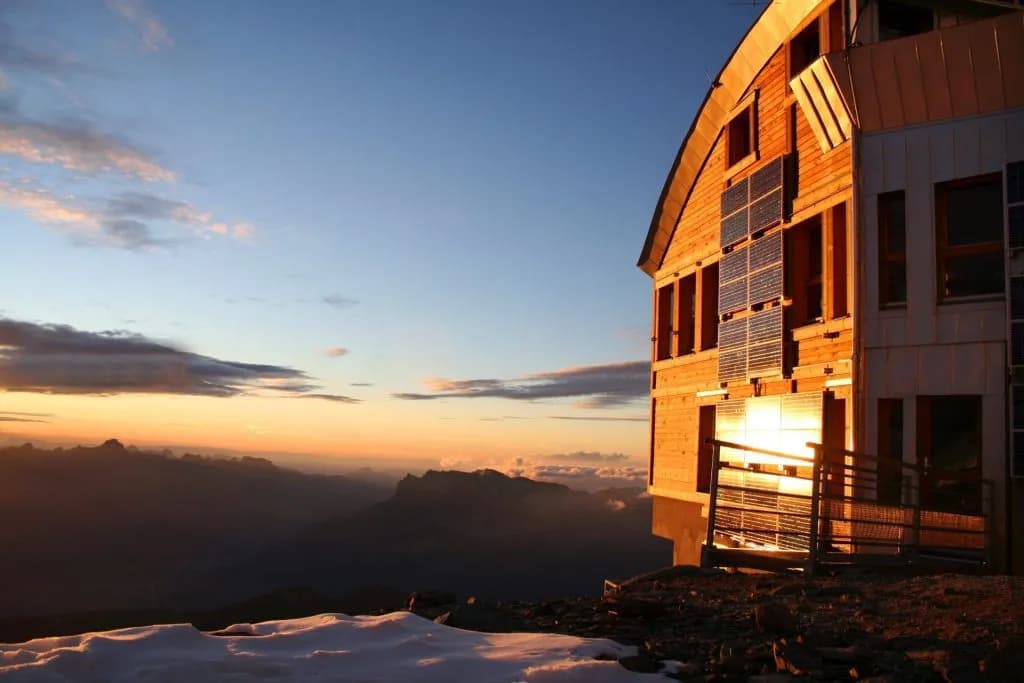 Tête Rousse Hut with solar panels at sunset overlooking alpine mountains and snow.