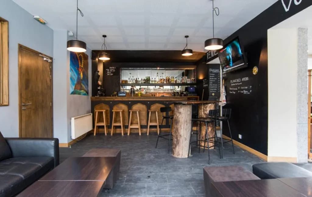 Bar interior with rustic wooden bar, black walls, modern seating, and liquor bottles on shelves.