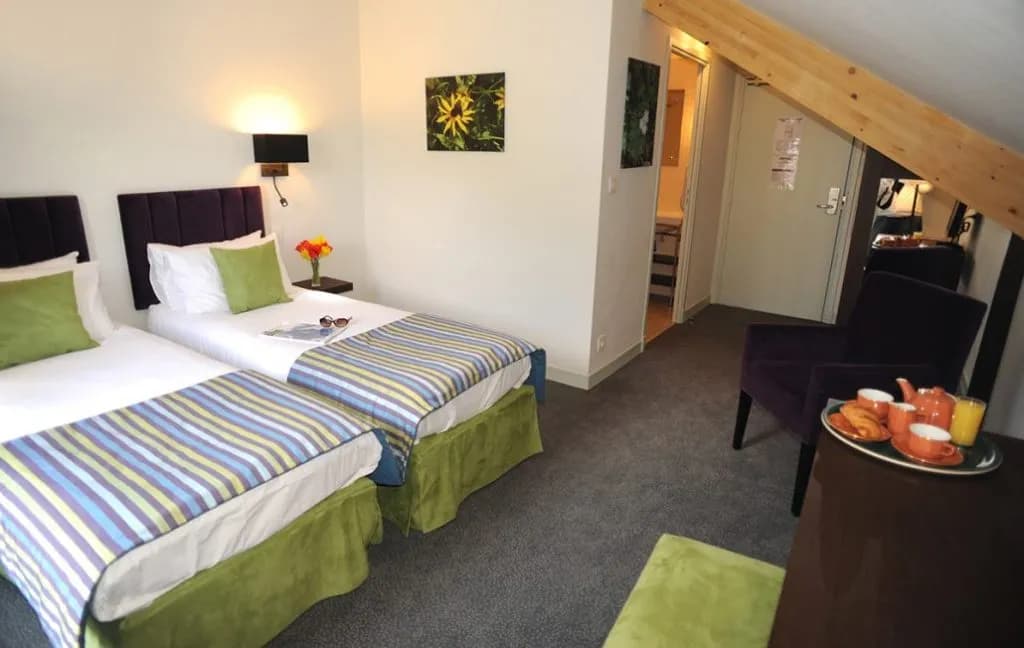 Twin beds with striped throws in a hotel room with an angled wooden ceiling beam.
