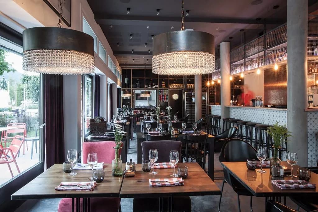 Dining room with crystal chandeliers, set tables, and a bar area looking out onto a patio.