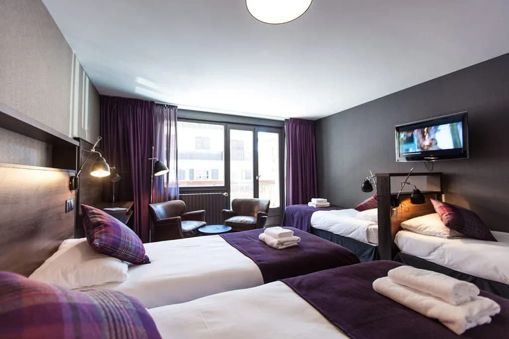 Quadruple hotel room with four single beds, purple accents, and a wall-mounted television
